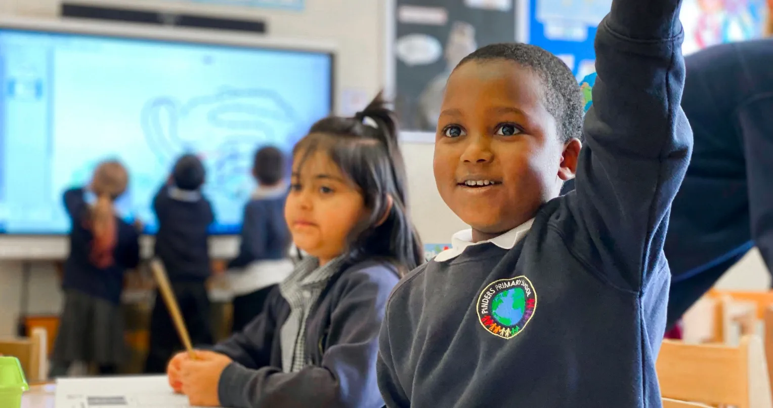 Two students at school with students engaging in an interactive display behind